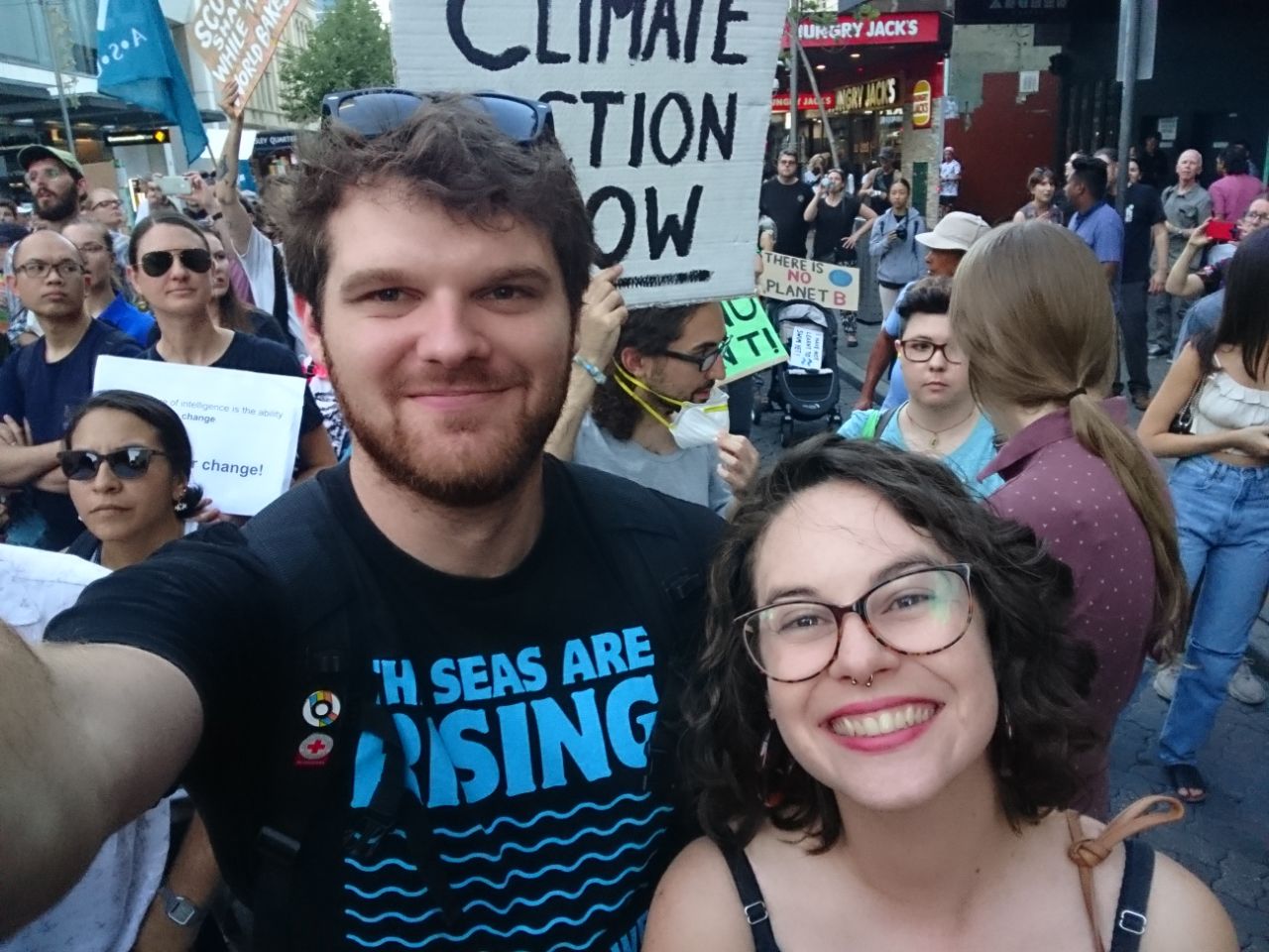 at a climate protest, with Liberty, wearing a shirt that says "the seas are rising and so are we".