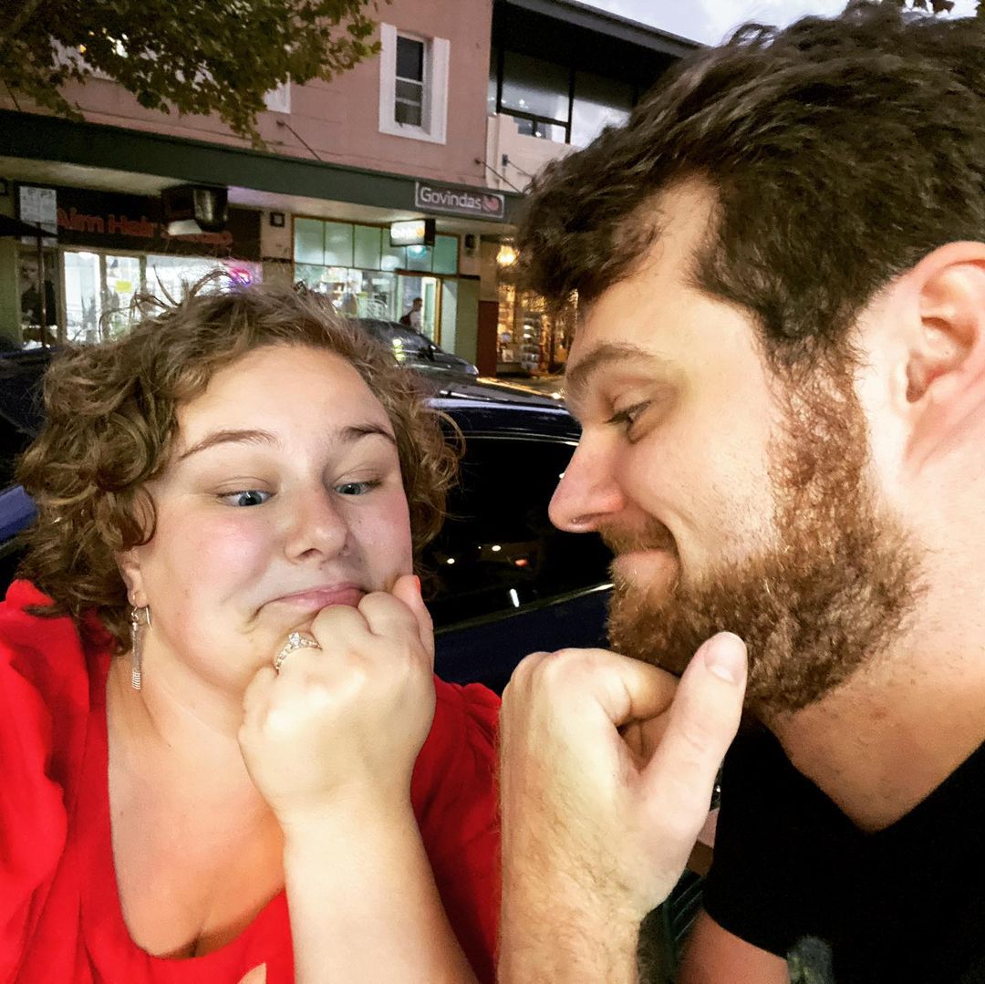 rocky and grace looking at an engagement ring on grace's finger like it somehow just appeared there by magic