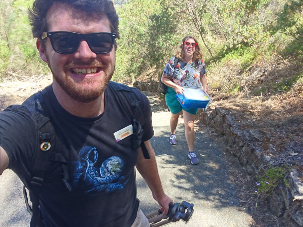 grinning, sweating, holding a tripod. Rose is in the background and is considerably less amused.