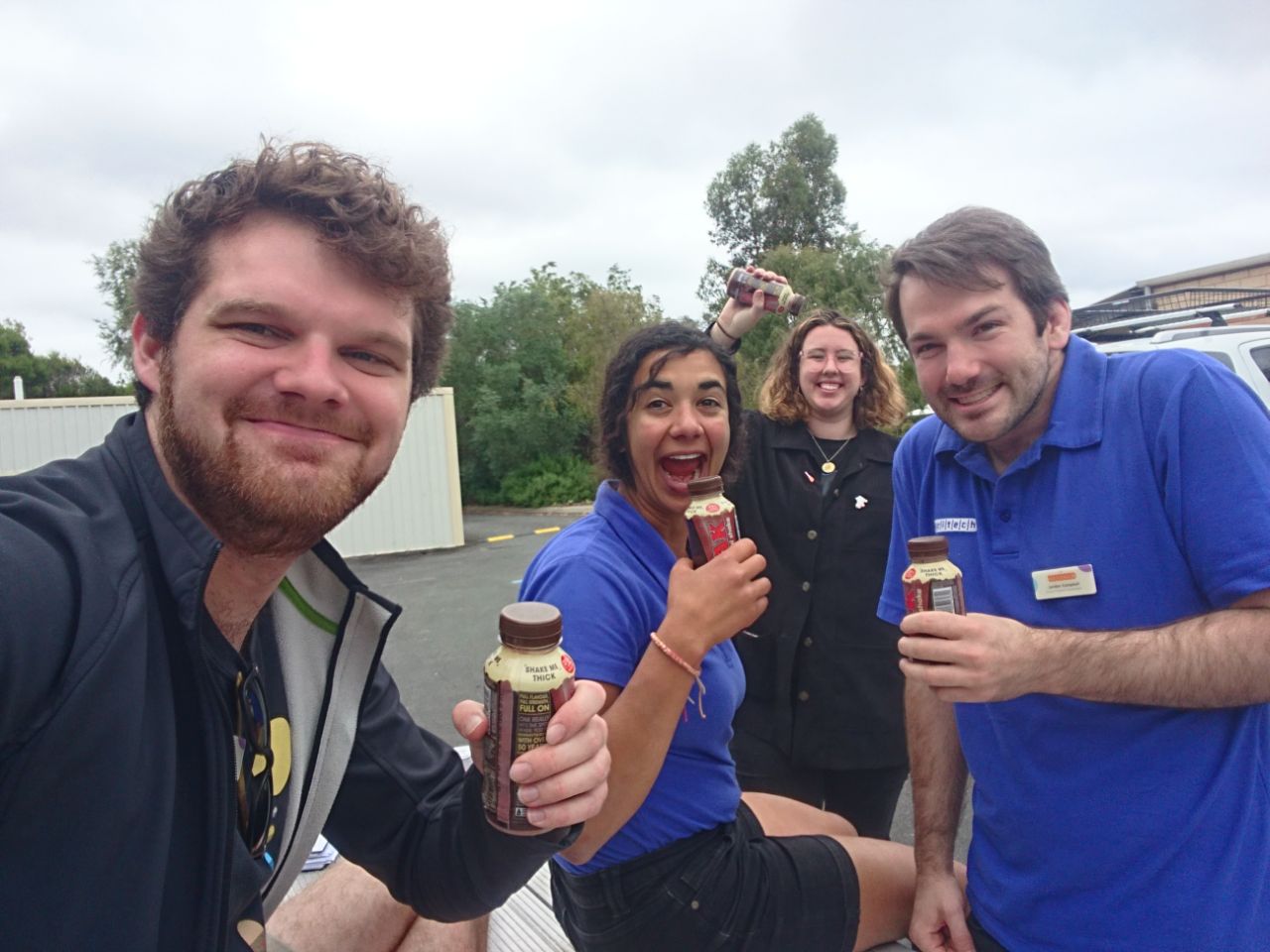 four grown adults acting like children in a primary school carpark because they are holding tiny milk bottles which were indeed intended for children