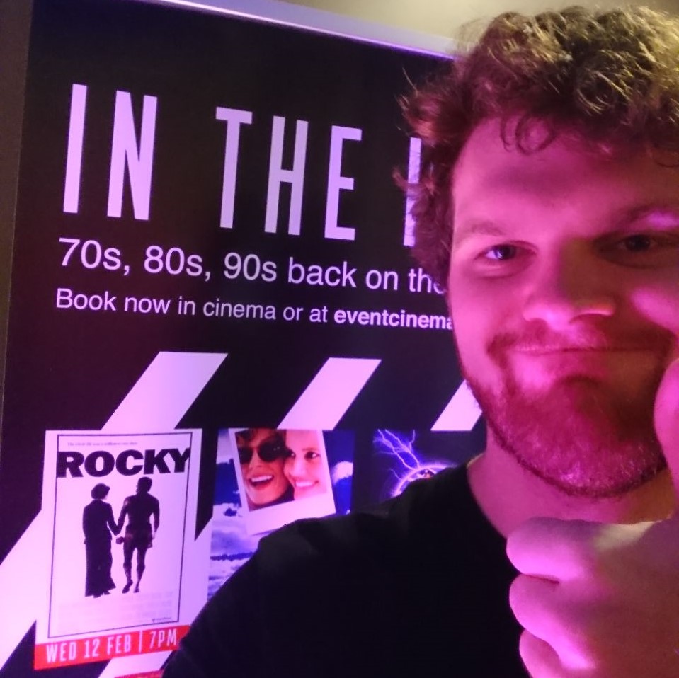 Doin' a thumbs up in front of a cinema poster for the film "Rocky"